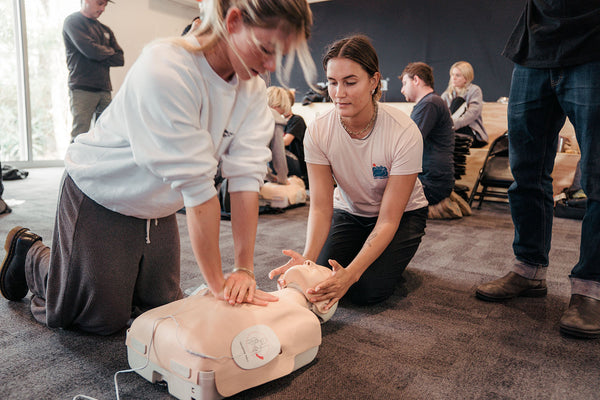 Two people practicing CPR on a mannequin in a classroom setting.